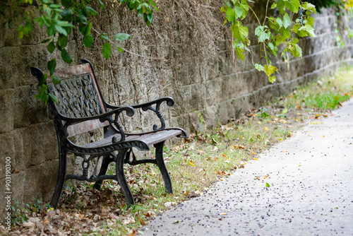 An empty bench sits next to sidewalk and retaining wall.