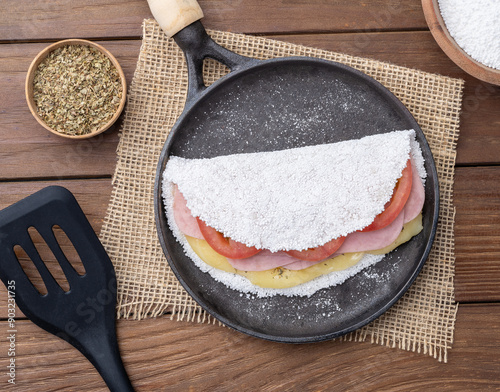 Traditional brazilian cheese, ham and tomato stuffed tapioca on a pan with ingredients photo