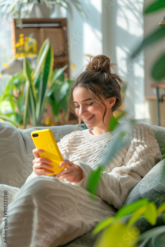 A young woman using her cell phone sitting on the sofa in her apartment, happy and joyful shopping online. photo