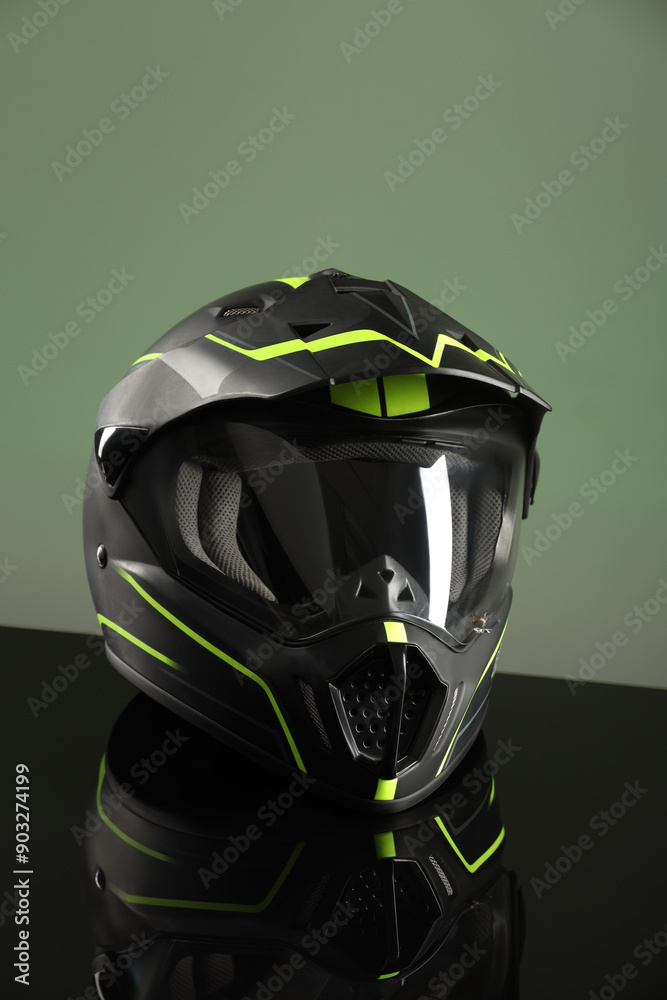 Modern motorcycle helmet with visor on mirror surface against light green background Modern motorcycle helmet with visor on mirror surface against light green background
