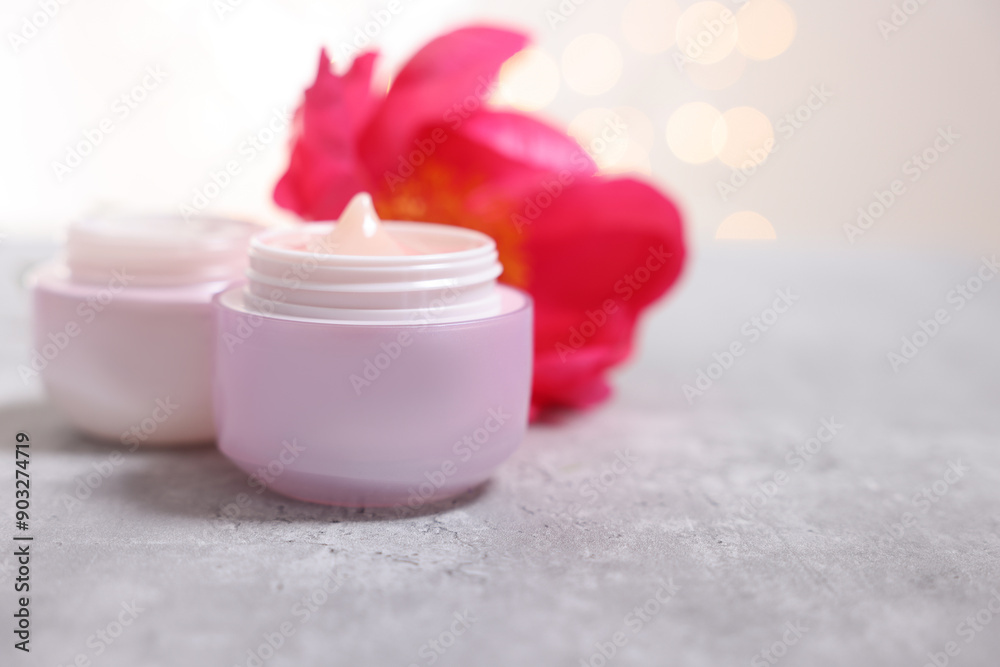 Jars of creams and peony flower on gray table against light background, closeup. Space for text Jars of creams and peony flower on gray table against light background, closeup. Space for text