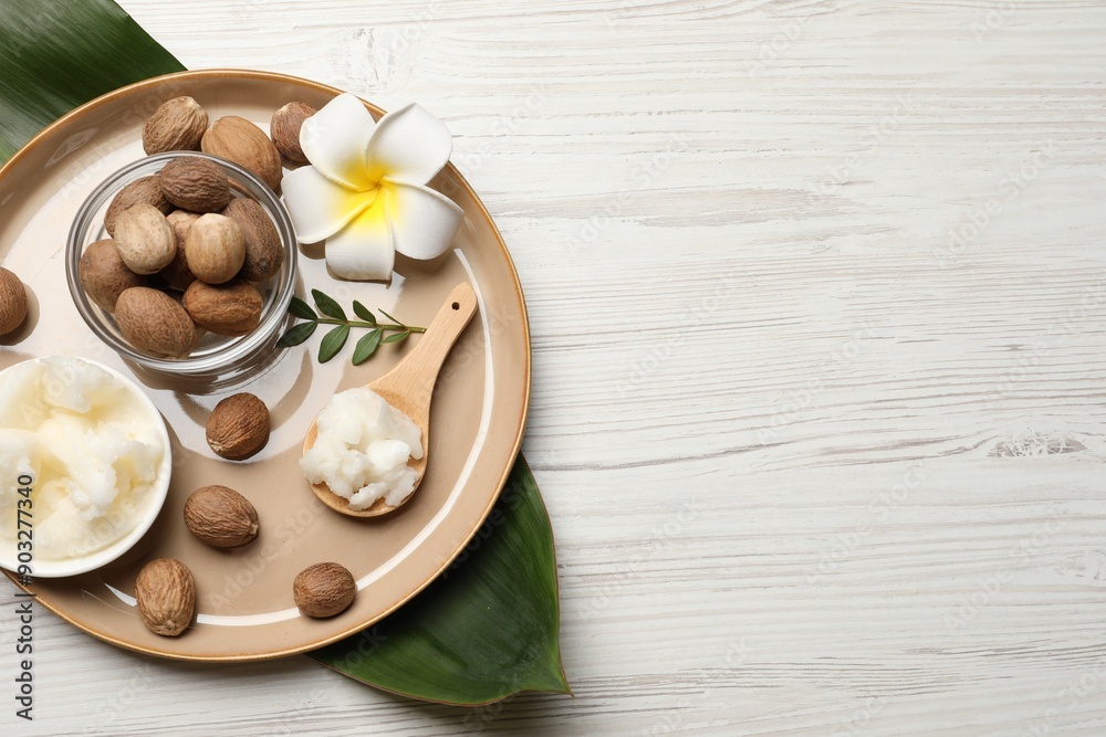 Natural shea butter in bowl, nuts, plumeria flower and green leaves on wooden table, top view. Space for text Natural shea butter in bowl, nuts, plumeria flower and green leaves on wooden table, top view. Space for text