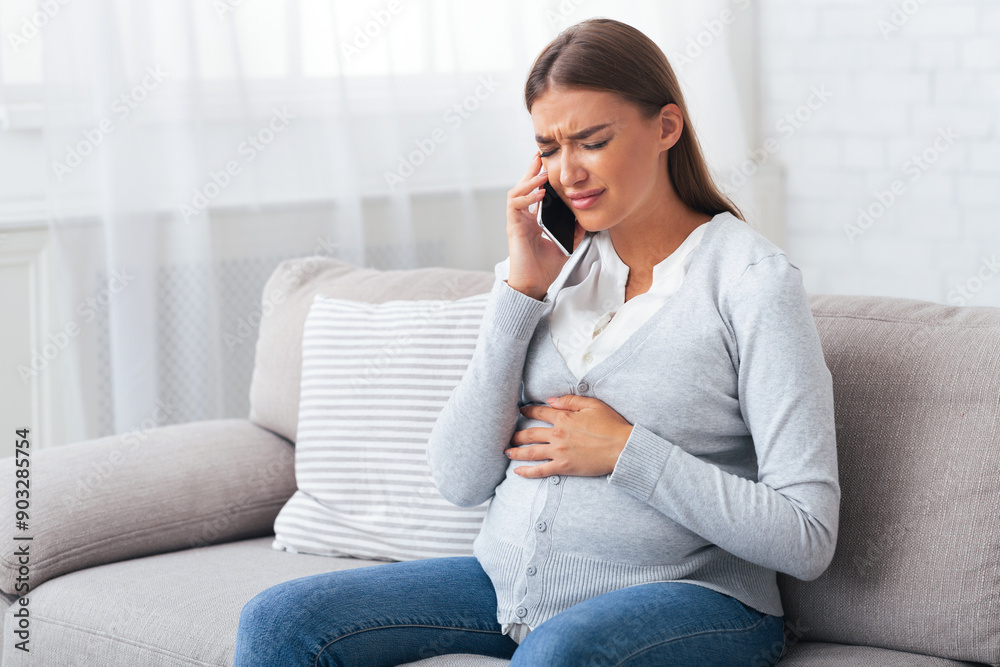 Emergency Call. Pregnant Girl Talking On Cellphone Feeling Bad Suffering From Pain Sitting On Sofa At Home. Emergency Call. Pregnant Girl Talking On Cellphone Feeling Bad Suffering From Pain Sitting On Sofa At Home.