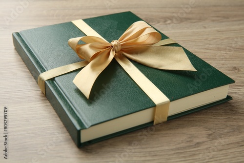 Book tied with golden ribbon on wooden table, closeup