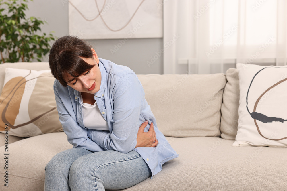 Upset woman suffering from abdominal pain on sofa at home Upset woman suffering from abdominal pain on sofa at home