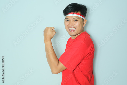 Indonesian man showing his arm muscle with enthusiastic expression. Wearing a red t-shirt