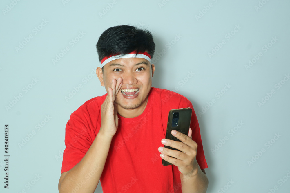 Indonesian man is holding a phone and shouting. The concept of Indonesia's independence day. Wearing a red t-shirt Indonesian man is holding a phone and shouting. The concept of Indonesia's independence day. Wearing a red t-shirt