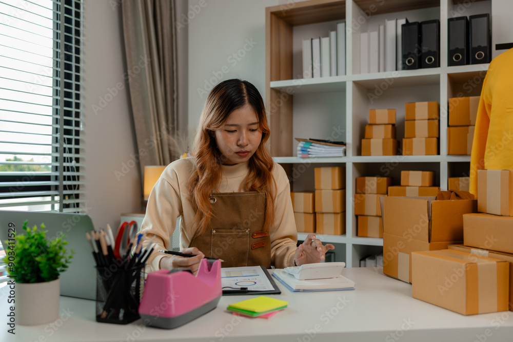 an entrepreneur or a business owner works in her office full of packages, it is a small business that she created with careful preparation, start up business of clothes an entrepreneur or a business owner works in her office full of packages, it is a small business that she created with careful preparation, start up business of clothes