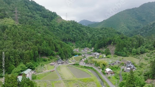 Car drives by houses and fields in Japan mountain village - Aerial