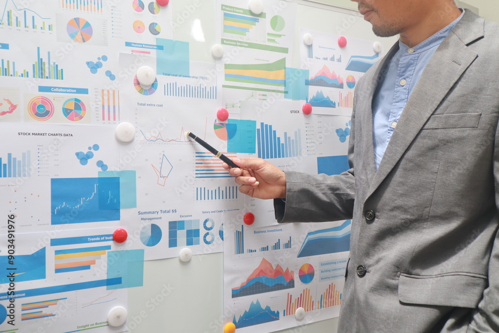 A confident businessman stands in an office, presenting ideas on a whiteboard. Dressed in a suit, he communicates strategies and concepts during a corporate meeting A confident businessman stands in an office, presenting ideas on a whiteboard. Dressed in a suit, he communicates strategies and concepts during a corporate meeting