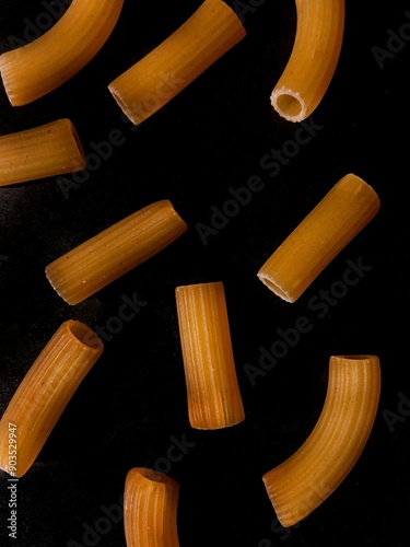 Dry Italian pasta cones on a black background. Dry pasta in close-up. The background is pasta, a place for text. Pasta tubes are the background for the text. Cooking. A carbohydrate diet.