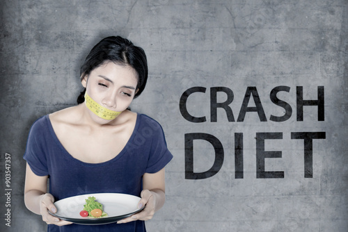 Diet concept. Young woman looks unhealthy while holding a plate of small portion salad