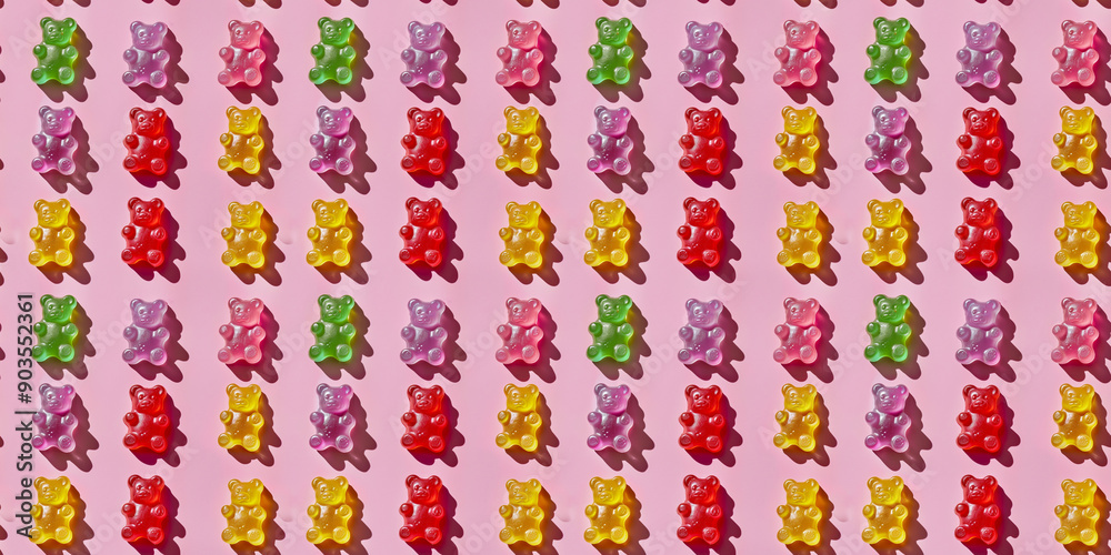A pattern of colorful gummy bear candies arranged in an orderly fashion on the pastel pink background, with shadows cast sunlight A pattern of colorful gummy bear candies arranged in an orderly fashion on the pastel pink background, with shadows cast sunlight