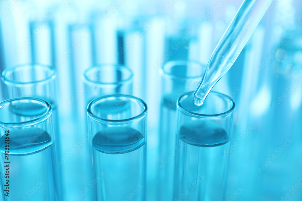 Dripping liquid from pipette into test tube on light blue background, closeup Dripping liquid from pipette into test tube on light blue background, closeup