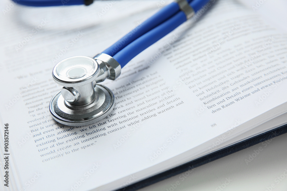 One medical stethoscope and book on white table, closeup One medical stethoscope and book on white table, closeup