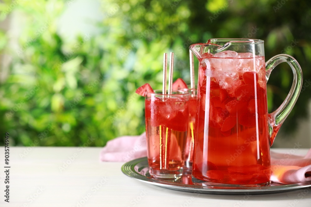 Tasty strawberry lemonade in jug and glasses on white table against blurred green background. Space for text Tasty strawberry lemonade in jug and glasses on white table against blurred green background. Space for text