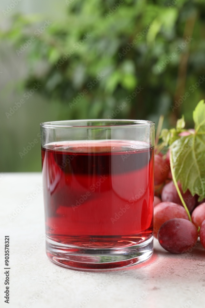 Tasty grape juice in glass, leaf and berries on light textured table against blurred green background, closeup Tasty grape juice in glass, leaf and berries on light textured table against blurred green background, closeup