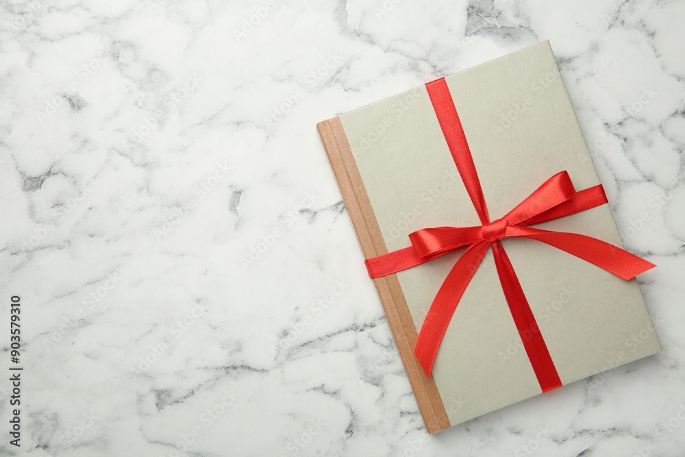 Book tied with red ribbon on white marble table, top view. Space for text