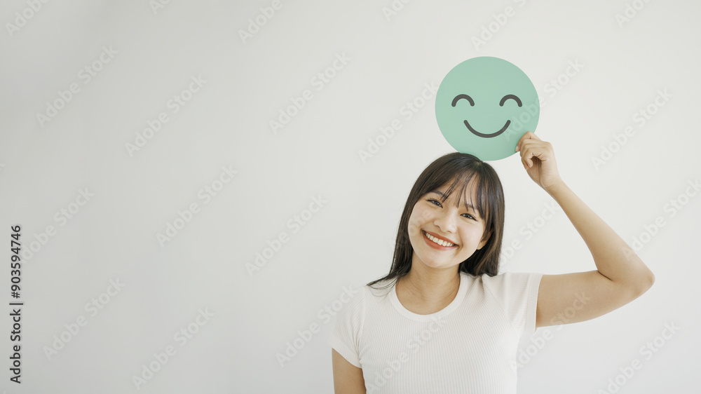 Happy young Asian woman holding smile emoji face, positive mental health, world mental health day concept Happy young Asian woman holding smile emoji face, positive mental health, world mental health day concept