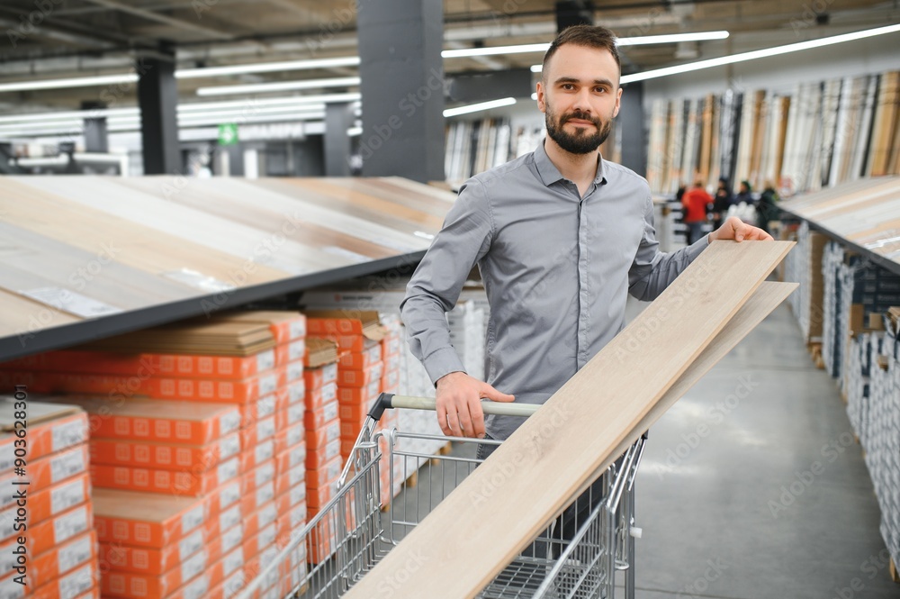 A young man chooses laminate flooring in the hardware store A young man chooses laminate flooring in the hardware store
