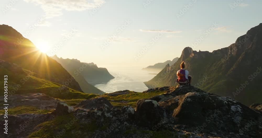 Woman overlook Senja fjord view from mountain in midnight sun glow; drone reveal
