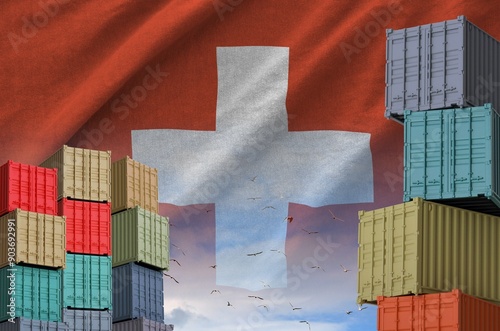 Switzerland flag and big stack of shipping cargo containers in docks with sky background close up