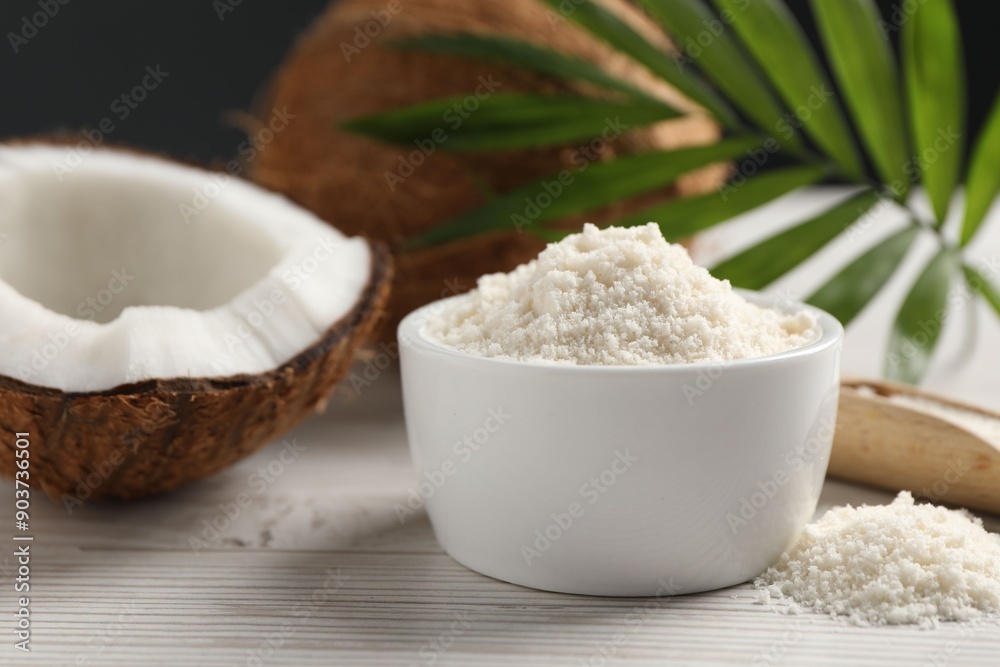 Fresh coconut flour in bowl, nuts and palm leaf on white wooden table Fresh coconut flour in bowl, nuts and palm leaf on white wooden table