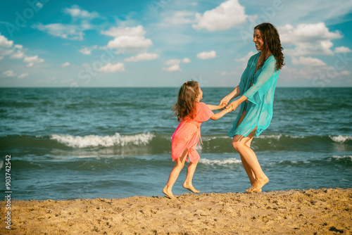 Young happy woman with little daughter dancing holding hands on the beach. Mother's Day concept