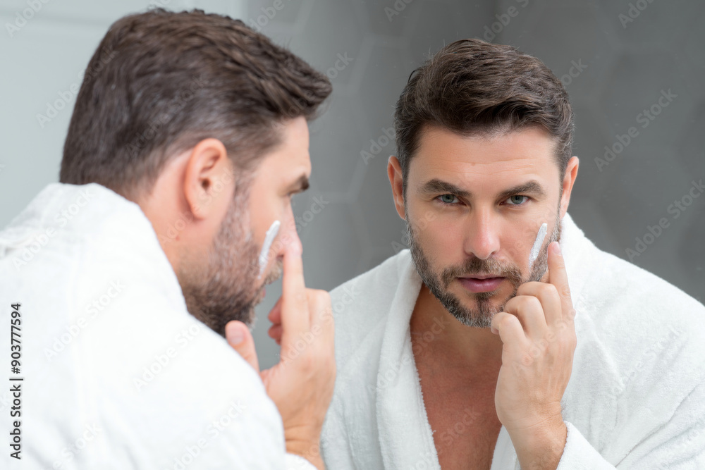 Fototapeta premium Skin care. Beauty middle aged man applying face cream. Male spa hold face cream. Facial cream, moisturizing lifting nourishing creme. Face cream for skincare. Wrinkle cosmetic facial treatment.