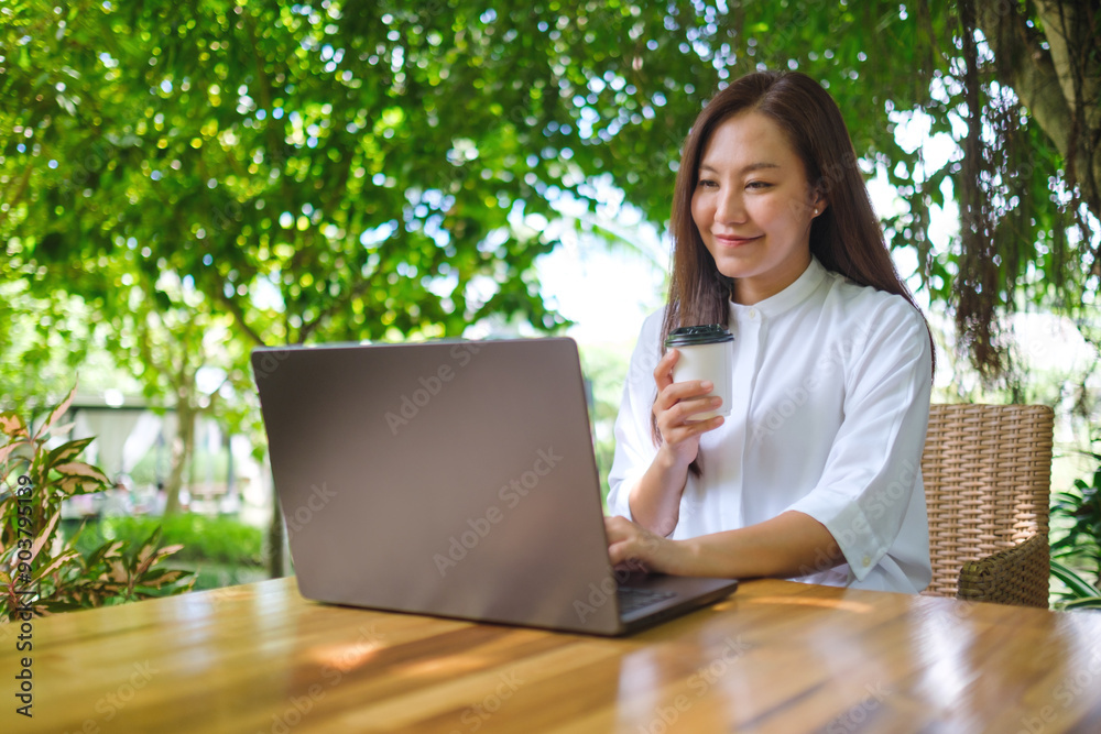 Portrait image of a woman drink coffee while working on laptop computer in the outdoors Portrait image of a woman drink coffee while working on laptop computer in the outdoors