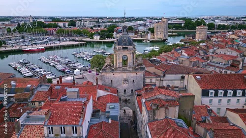 The big clock or grosse horloge at old port and chain and Saint Nicolas towers in background, La Rochelle, France. Aerial drone sideways photo