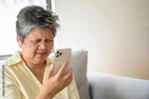 фотографія Senior people lifestyle health problem concept : Portrait photo of senior Asian woman has an eye long sighted problem trying to read message from smartphone monitor