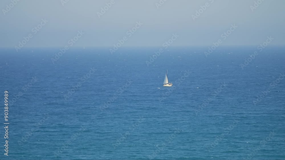 Single-sail boat on choppy sea, waves slightly foamy. Only a jib sail visible. Man fighting the water's force. Slow-motion video.