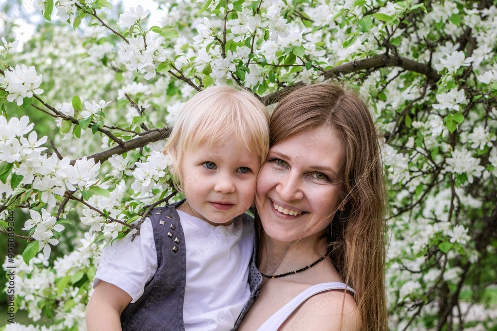 Smiling beautiful mother and her child are standing in a blossoming garden. Happy family together. Smiling beautiful mother and her child are standing in a blossoming garden. Happy family together.