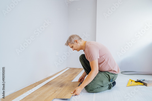 Young handyman installing flooring in new Home by his own. Doing measurements, calculating for vinyl laminate and skirting. DIY, Do it yourself. Home renovation, improvement, refurbishment.