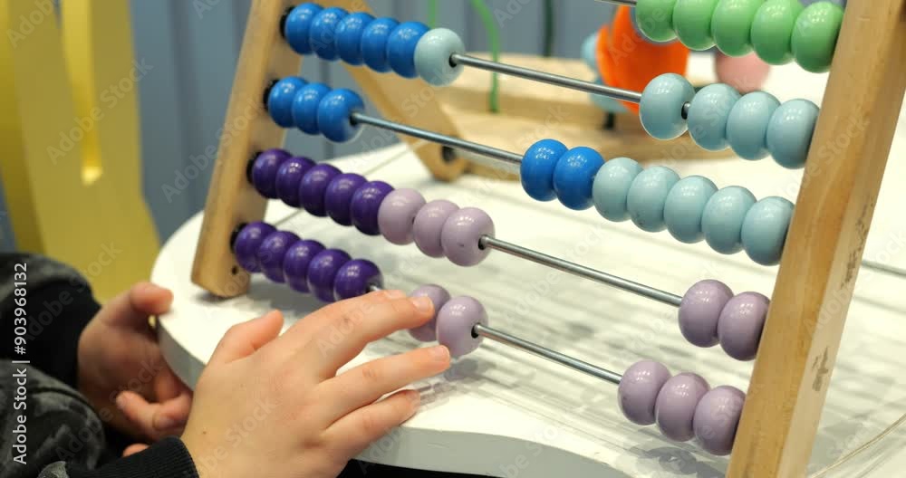 Little child solves maths tasks moving colorful beads on abacus at desk closeup. Toddler boy learns to count with old-fashioned device in preschool class Little child solves maths tasks moving colorful beads on abacus at desk closeup. Toddler boy learns to count with old-fashioned device in preschool class