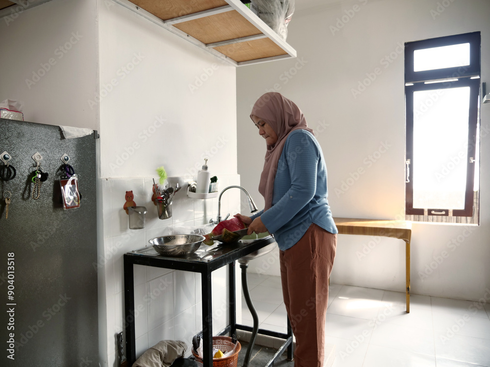 Asian muslim woman cutting slicing watermelon fruits in kitchen Asian muslim woman cutting slicing watermelon fruits in kitchen