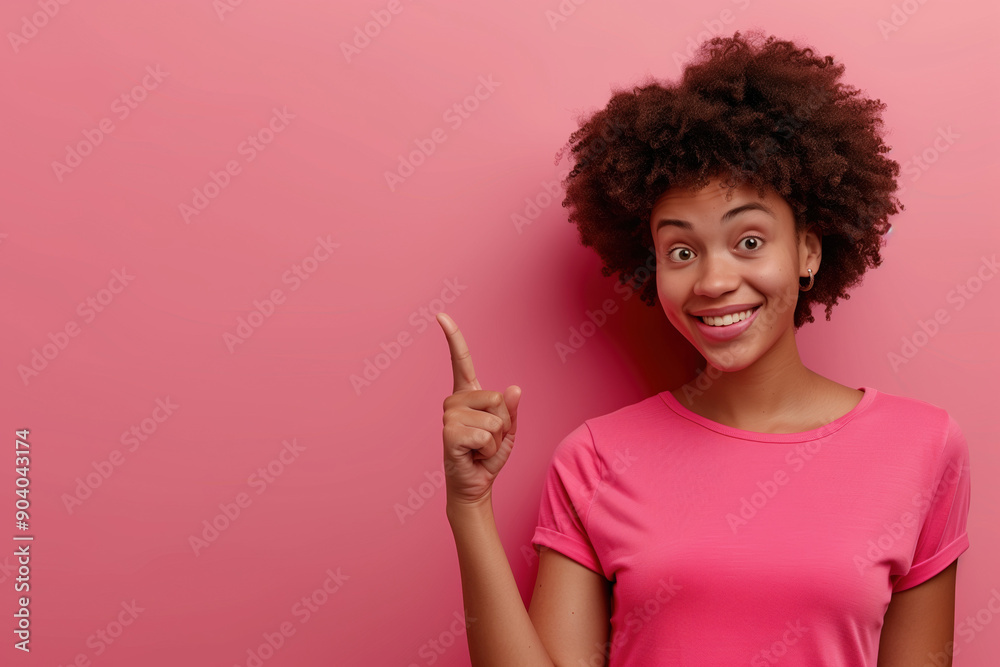 Young woman with bright smile pointing upwards against soft pink background during daytime Young woman with bright smile pointing upwards against soft pink background during daytime