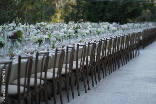 A picturesque outdoor dining setting with a long table adorned with white floral arrangements and greenery