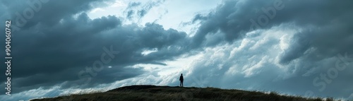 Lone figure standing on a hill under dramatic cloudy sky, capturing solitude and adventure in nature's vast landscape.