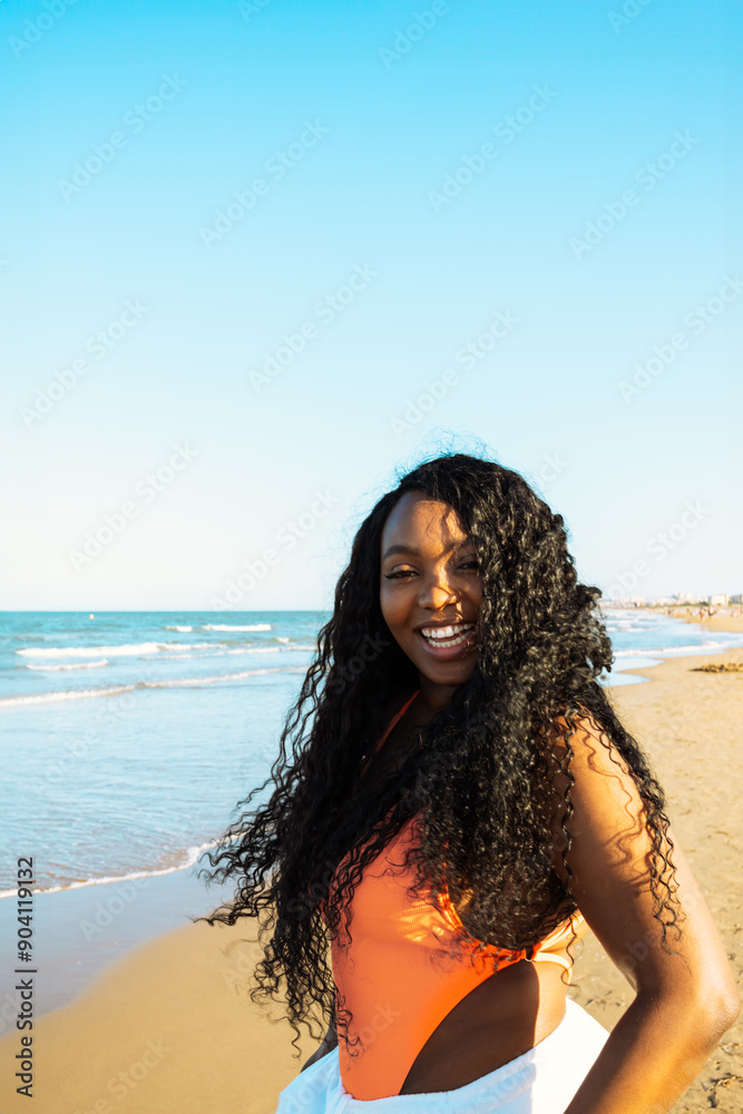 Curly smiling african american dark skinned woman walking on sea water in white pants and swimsuit. Mixed race people, ethnicity, diversity. Curly smiling african american dark skinned woman walking on sea water in white pants and swimsuit. Mixed race people, ethnicity, diversity.