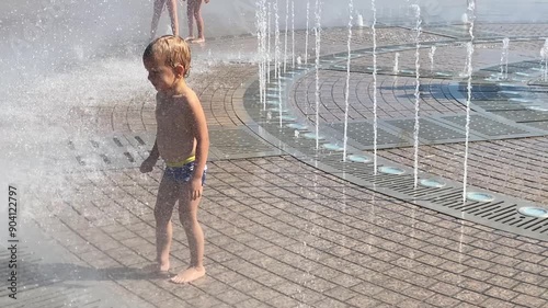 Happy wet child run barefoot bathing in fountain water streams in summer. Light and music fountain on the Tereshkova embankment. Yevpatoria, Crimea, Russia 2024 photo