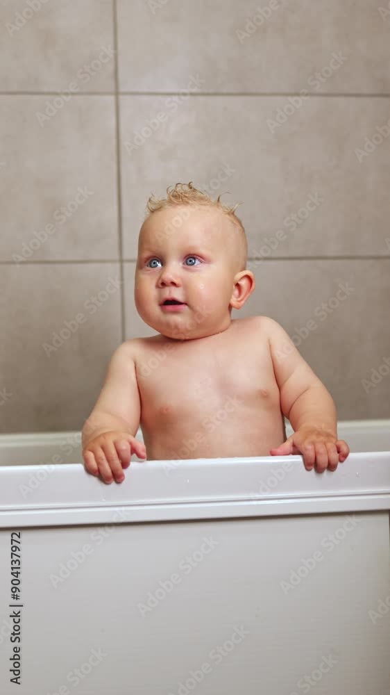 A cute blue-eyed 1-year-old boy is bathing in a white bath. Baby's personal hygiene. A child with a smile on his face while bathing. Vertical video A cute blue-eyed 1-year-old boy is bathing in a white bath. Baby's personal hygiene. A child with a smile on his face while bathing. Vertical video