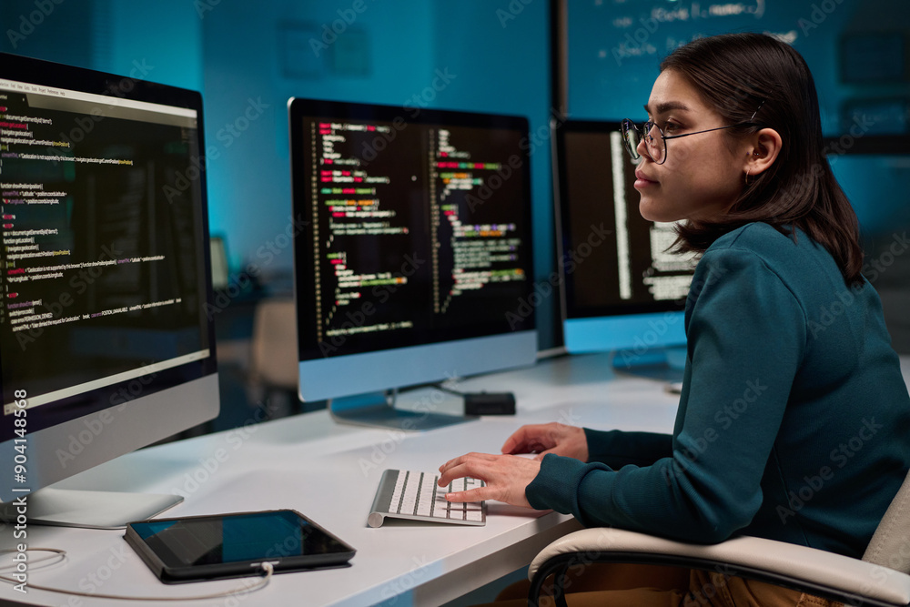 Side view portrait of female computer programmer typing at keyboard and writing code at office workplace copy space Side view portrait of female computer programmer typing at keyboard and writing code at office workplace copy space