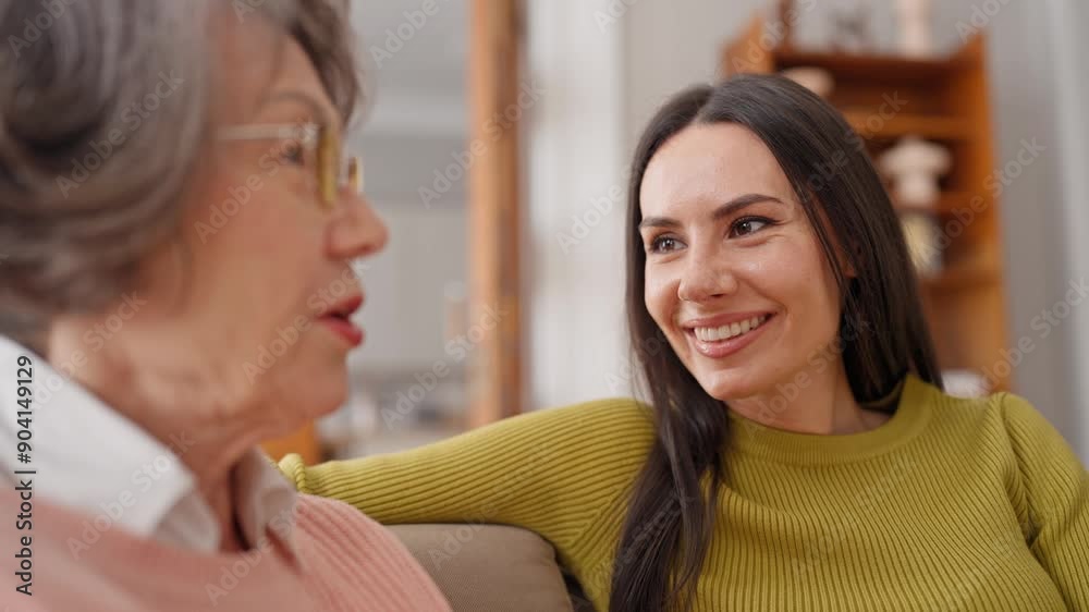 Camera fucus on Caucasian young woman with dark hair attentively listening to her mother. Two women having cheerful conversation. Adult mom telling about home routine to daughter. Feeling happy. Camera fucus on Caucasian young woman with dark hair attentively listening to her mother. Two women having cheerful conversation. Adult mom telling about home routine to daughter. Feeling happy.