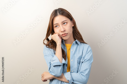 Young female brunette hair in yellow shirt thoughtful isolated on background.