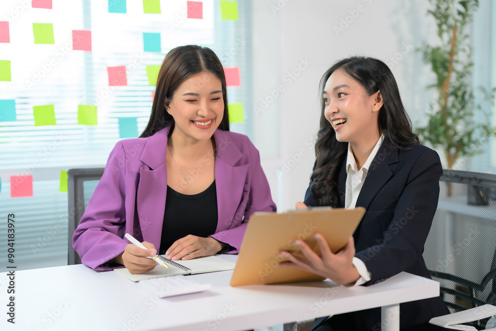 Two Businesswomen Collaborating in Modern Office with Sticky Notes on Glass Wall, Discussing Project on Tablet Two Businesswomen Collaborating in Modern Office with Sticky Notes on Glass Wall, Discussing Project on Tablet