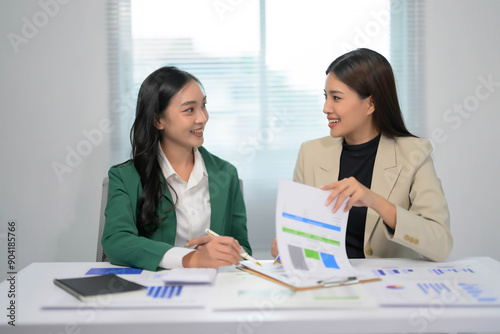 Two Businesswomen Discussing Financial Reports in a Modern Office Setting with Natural Light