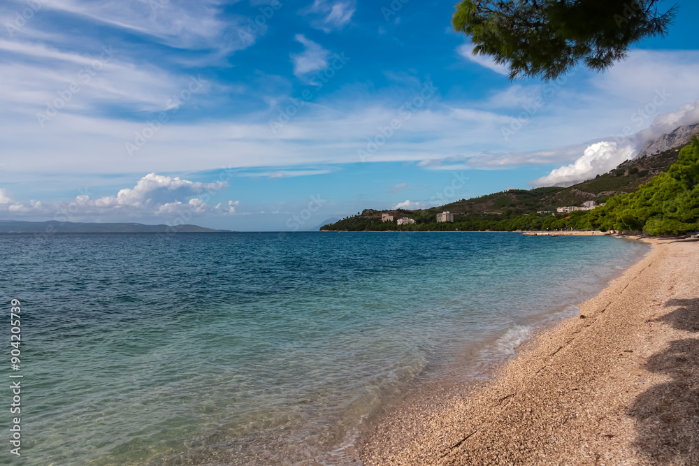 Fototapeta premium Serene coastal scene in tourist town Tucepi along Makarska Riviera, Dalmatia, Croatia, Europe. Pristine pebble beach stretches towards calm, turquoise Adriatic sea in the Mediterranean. Summer travel