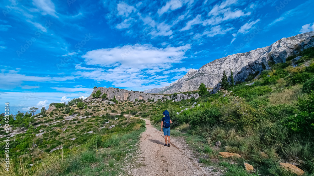 Hiker man with baby carrier backpack on idyllic hiking path to Tucepi town along Makarska Riviera, Dalmatia, Croatia, Europe. Majestic Biokovo mountains rise up against dramatic sky. Dinaric Alps Hiker man with baby carrier backpack on idyllic hiking path to Tucepi town along Makarska Riviera, Dalmatia, Croatia, Europe. Majestic Biokovo mountains rise up against dramatic sky. Dinaric Alps
